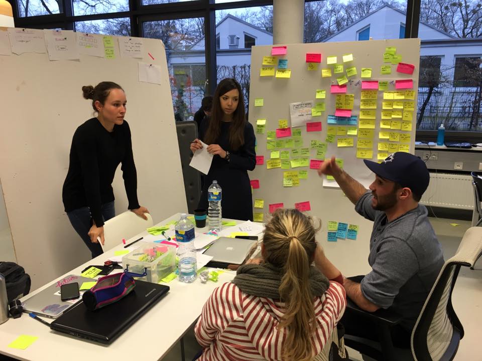 Group of four students in a brainstorming session with a whiteboard filled with sticky notes